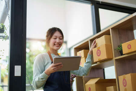 A portrait of a small startup, an SME owner, an Asian female entrepreneur checking orders to arrange the produce before packing the products in the inner boxes with the customers. Freelance concepts.の写真素材