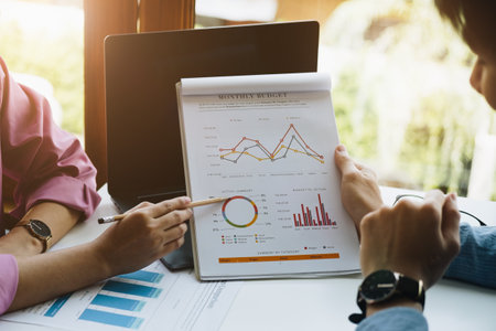 Negotiation, Analysis, Discussion, Asian woman economist and marketer pointing to a financial data sheet to plan investments to prevent risks and losses for the company.の写真素材