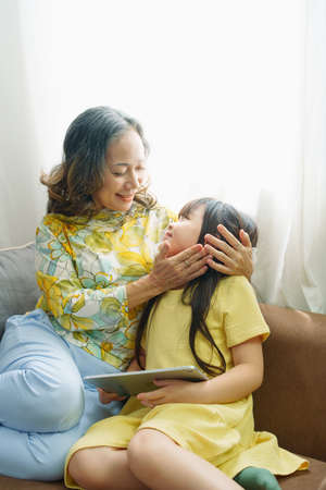 Asian portrait, Grandma and granddaughter doing recreational activities playing tablet computers on the sofa.の写真素材