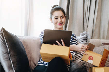 Online merchandising business idea, beautiful girl using ipad to check orders to deliver parcels to customers according to orders received from customersの写真素材