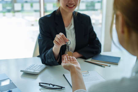 Accountant, businessman, real estate agent, Asian business woman handing keys to customers along with house after customers to sign.の写真素材