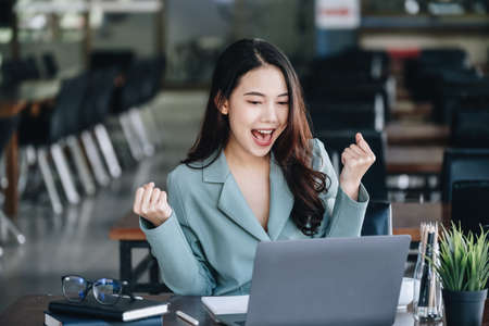 Business finance and investment, a business woman expresses happiness after successfully investing in the stock market on the Internet through a computer placed on a deskの写真素材