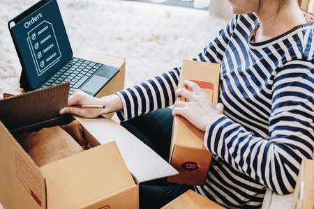 Online merchandising business idea, a beautiful girl is packing the products in the parcel box from...