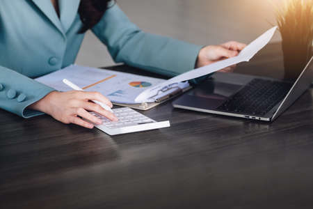 Financial and investment auditing concept, female auditor is pressing calculator to check budget and correctness of company profits through paperwork to calculate annual taxの写真素材