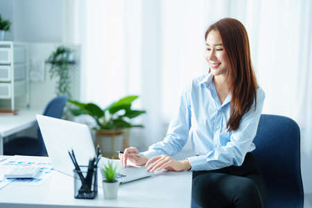 An Asian entrepreneur or businesswoman shows a smiling face while working with using computer on a wooden tableの写真素材