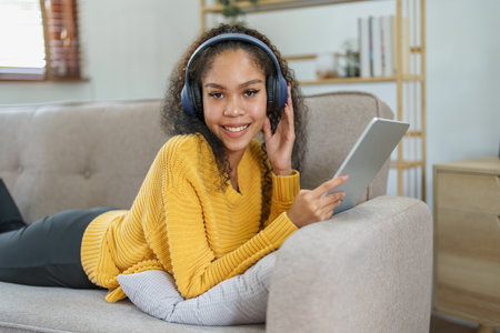 Portrait of an African American sitting on a sofa using tablet and wearing headphones to relax.の写真素材