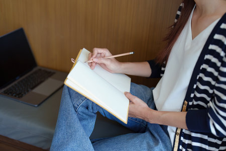 Portrait of a young Asian teenage girl in love wearing headphones, using a notebook and computer to...