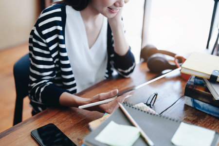 A portrait of a young Asian woman with a smiling face using a tablet computer during an online video conferencing class in a library.の写真素材