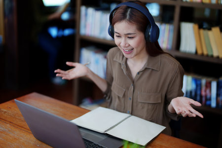 Portrait of a smiling Asian teenage girl wearing headphones and using a computer for online video...