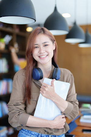 A portrait of a young Asian woman with a smiling face looking for a textbook in the library.の写真素材