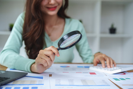 A half-bred girl, an audit employee, an accountant holding a magnifying glass and using a calculator to check the financial statement documents to calculate the annual tax payment to the IRS.の写真素材
