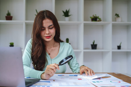A half-bred girl, an audit employee, an accountant holding a magnifying glass and using a calculator to check the financial statement documents to calculate the annual tax payment to the IRS.の写真素材