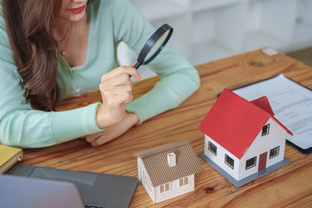 The client holds a magnifying glass to select a house model, inspect the concept of a home before making a decision to invest, make a loan, get insurance and sign important documents with the bankの写真素材