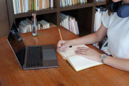 Portrait of a teenage Asian woman using a computer and notebook to study online via video...