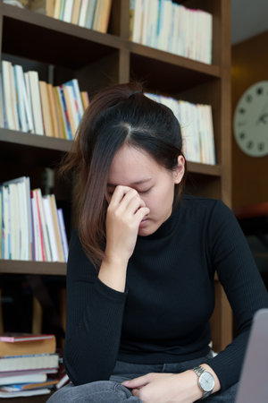 A portrait of a young Asian woman using a computer, wearing headphones and using a notebook to study...