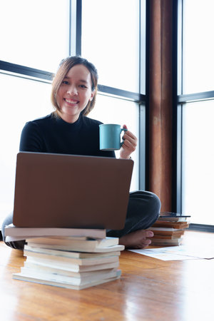 Portrait of an Asian woman using a computer to study online and drinking coffee while video...