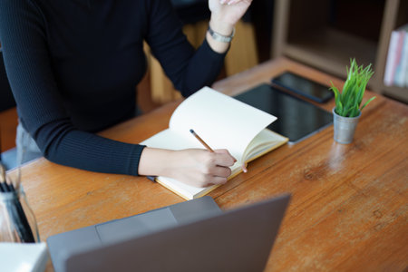 Portrait of a teenage Asian woman wearing glasses using computer laptop, headphones and using a laptop to study online via video conferencing on a wooden library table.の写真素材