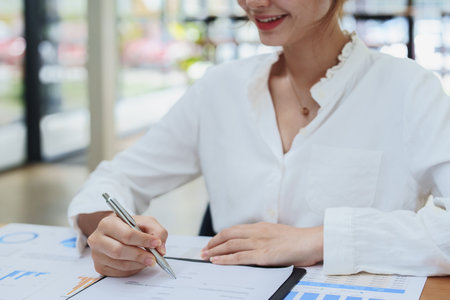 Portrait of a beautiful female employee holding a pen, using a computer and checking the companys budget documentsの写真素材