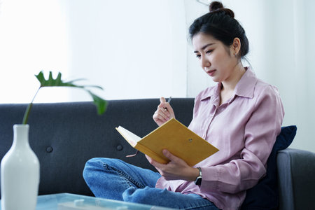 Portrait of a self-employed Asian woman holding a notebook and using a computer doing video conference at home.の写真素材