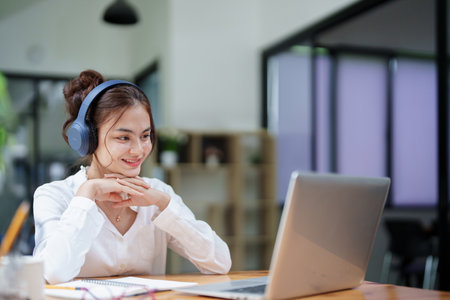 Portrait of a beautiful woman using a computer and earphone during a video conferenceの写真素材