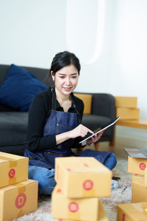 Startup small business entrepreneur of freelance Asian woman smiling and using tablet computer with Cheerful success of item online marketing packaging box and delivery SME idea concept.の写真素材