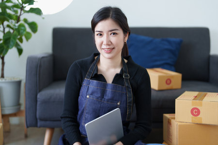 Startup small business entrepreneur of freelance Asian woman smiling and using tablet computer with Cheerful success of item online marketing packaging box and delivery SME idea concept.の写真素材