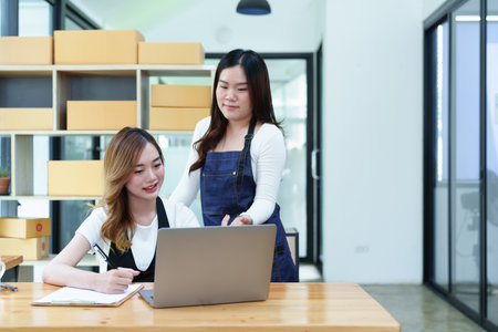 Starting small business entrepreneur of independent Asian woman smiling using computer laptop with cheerful success of online marketing package box items and SME delivery concept.の写真素材