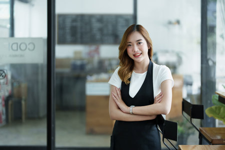 Starting and opening a small business, a young Asian woman showing a smiling face in an apron standing in front of a coffee shop bar counter. Business Owner, Restaurant, Barista, Cafe, Online SME.の写真素材