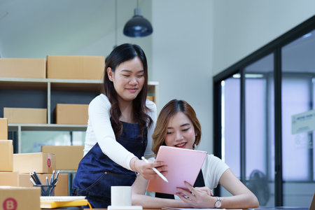 Starting small business two entrepreneur of independent Asian woman smiling using computer laptop with cheerful success of online marketing package box items and SME delivery concept.の写真素材