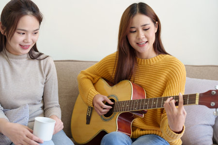 LGBTQ concepts, female couple playing guitar happily on the sofa in the house.の写真素材