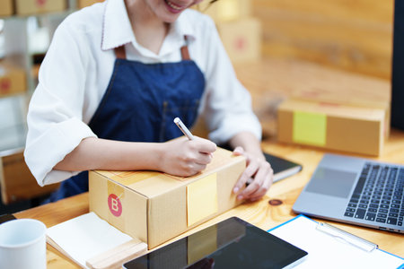 Starting small business entrepreneur of independent Asian woman smiling using computer laptop with cheerful success of online marketing package box items and SME delivery concept.の写真素材