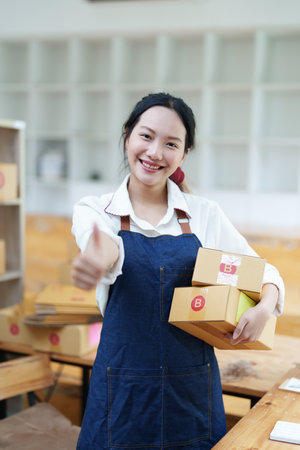 Starting small business entrepreneur of independent Asian woman smiling using computer laptop with cheerful success of online marketing package box items and SME delivery concept.の写真素材