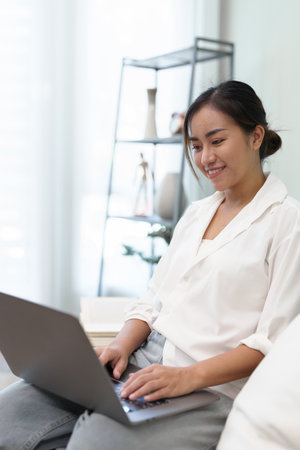 Portrait of a young Asian woman sitting on the sofa using a computerの写真素材