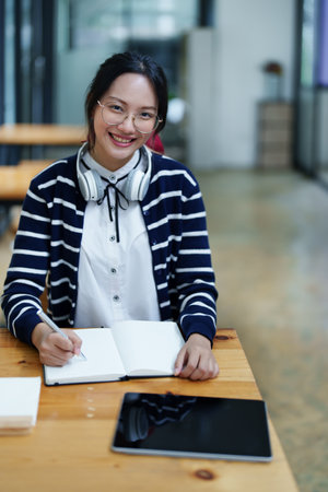 Portrait of a beautiful young Asian student using a notebook to take notes in the library.の写真素材