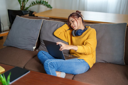 Portrait of a young Asian woman using a computer on the sofa.の写真素材