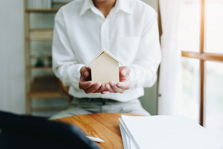 Accountant, businessman, real estate agent, Asian business man handing model house to customers along with house interest calculation documents for customers to sign.の写真素材