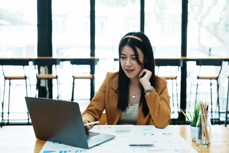 Portrait of a thoughtful Asian businesswoman looking at financial statements and making marketing plans using a computer on her desk.の写真素材