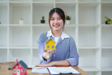 Accountant, businesswoman, real estate agent, Asian business woman handing model house and keys to customers along with house interest calculation documents for customers to sign.の写真素材