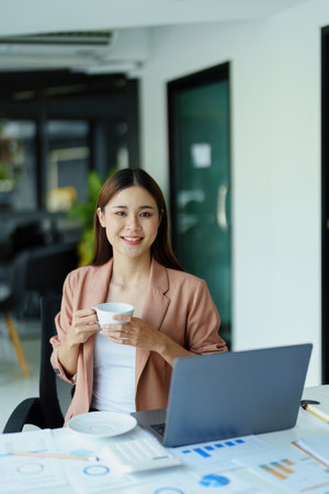Portrait of a woman taking a coffee break while using a computerの写真素材