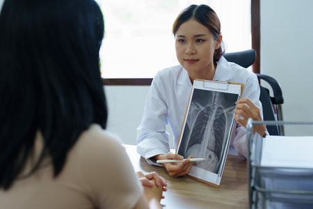 An Asian female doctor points to a patient x-ray film to explain the patients treatment process.