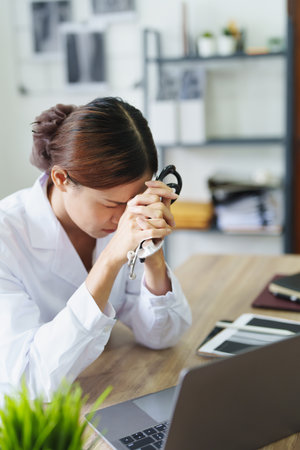 An Asian female doctor uses a computer while showing concern about patient information.の写真素材