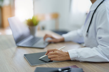 Portrait of an Asian female doctor using a computer and tablet to work.