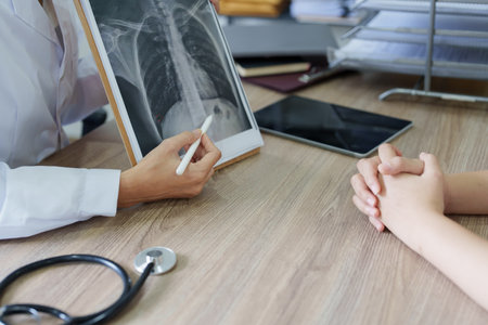 An Asian female doctor points to a patient x-ray film to explain the patients treatment process.の写真素材