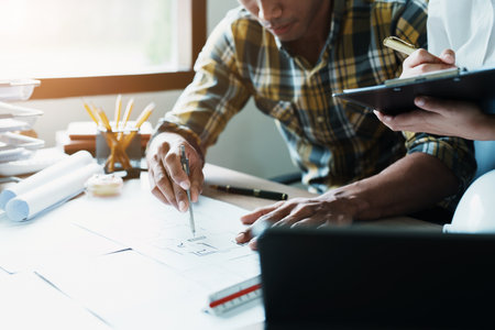 Engineers are consulting the team to design an architectural structure for clients with blueprints and building models to work at office.の写真素材