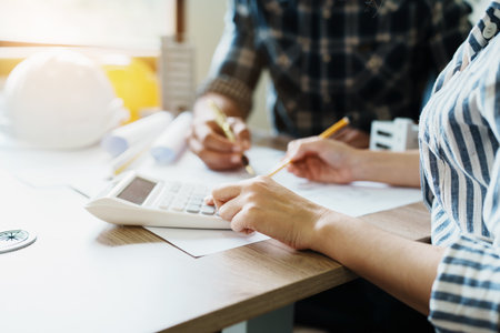 Engineers are consulting the team to design an architectural structure for clients with blueprints and building models to work at office.の写真素材