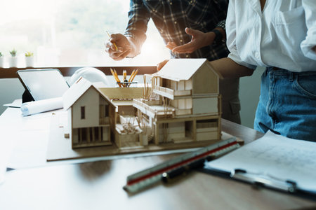 Engineers are consulting the team to design an architectural structure for clients with blueprints and building models to work at office.の写真素材