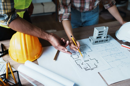 Engineers are consulting the team to design an architectural structure for clients with blueprints and building models to work at office.の写真素材