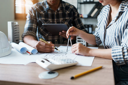 Engineers are consulting the team to design an architectural structure for clients with blueprints and building models to work at office.の写真素材