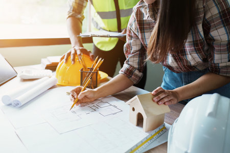 Engineers are consulting the team to design an architectural structure for clients with blueprints and building models to work at office.の写真素材