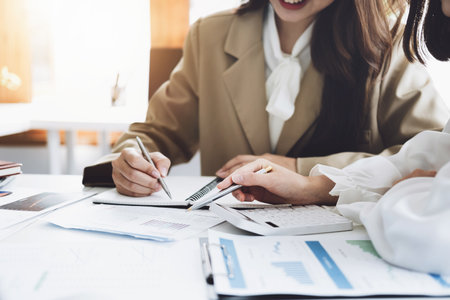 Negotiation, Analysis, Discussion, Asian woman economist and marketer pointing to a financial data sheet to plan investments to prevent risks and losses for the company.の写真素材